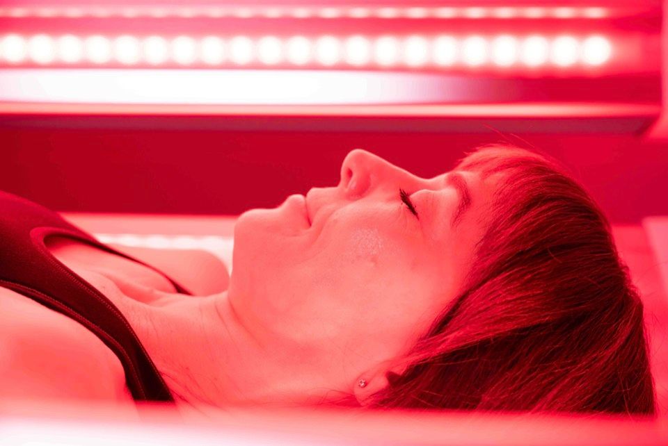 A client resting with eyes closed under the red light panels, seen in profile