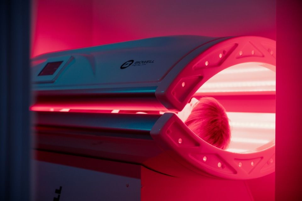 The Biowell red light bed open at one end, its tubes lit, with a client inside